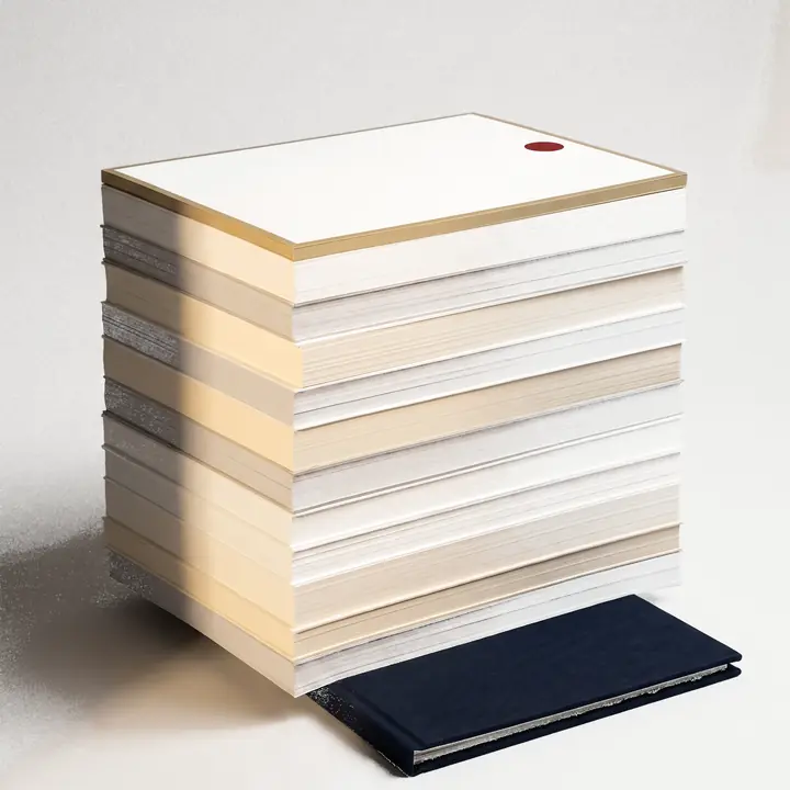 A tall stack of blank layered paper with a gold edge, resting on a navy folder in morning light